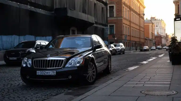 A luxurious black Maybach car parked on a cobblestone street in an urban setting at sunset.