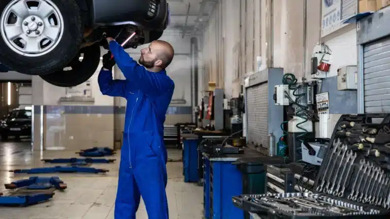 Mechanic inspecting a raised car in an auto workshop for maintenance and repair services.
