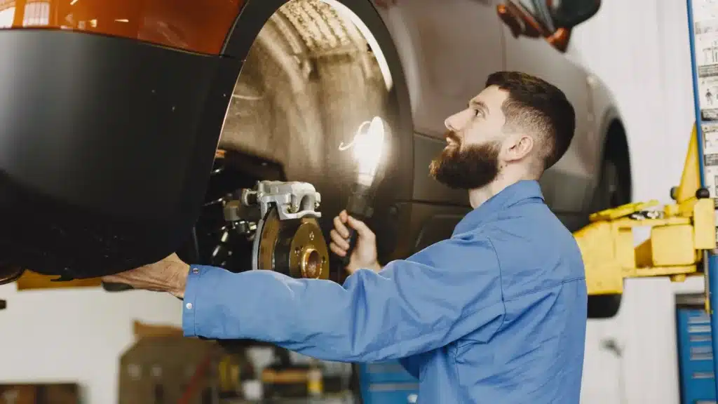 Professional mechanic in blue coveralls inspecting car brakes in a well-lit garage.