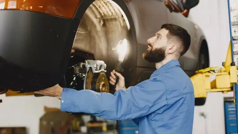 Professional mechanic in blue coveralls inspecting car brakes in a well-lit garage.