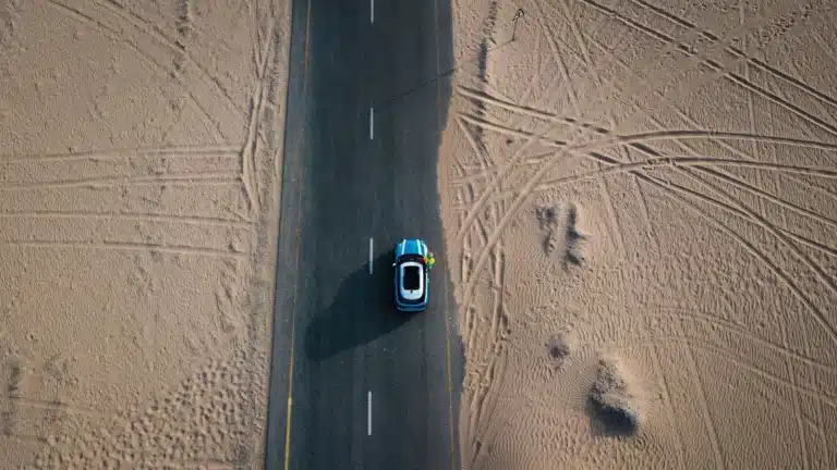 Aerial shot of a car driving on a road through the Dubai desert, showcasing travel and adventure.