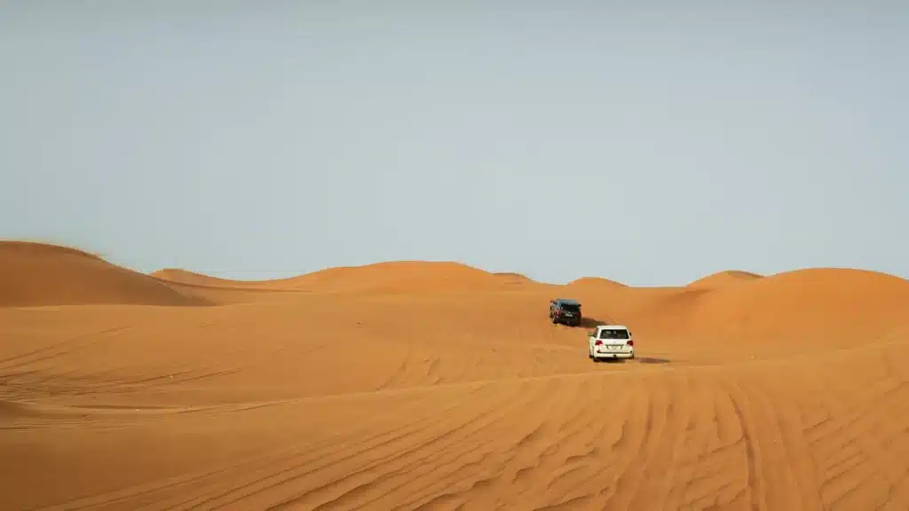 SUVs tread the stunning golden dunes of Dubai under a clear sky, capturing the essence of adventure.