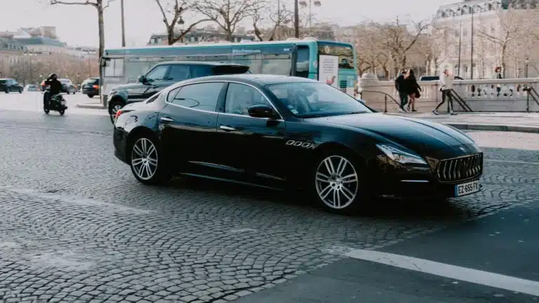Sleek black car driving on a European city street in daylight, capturing elegance and urban life.