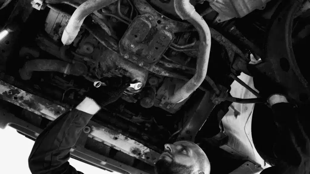 Mechanic performing repair on a vehicle's undercarriage in a garage workshop.