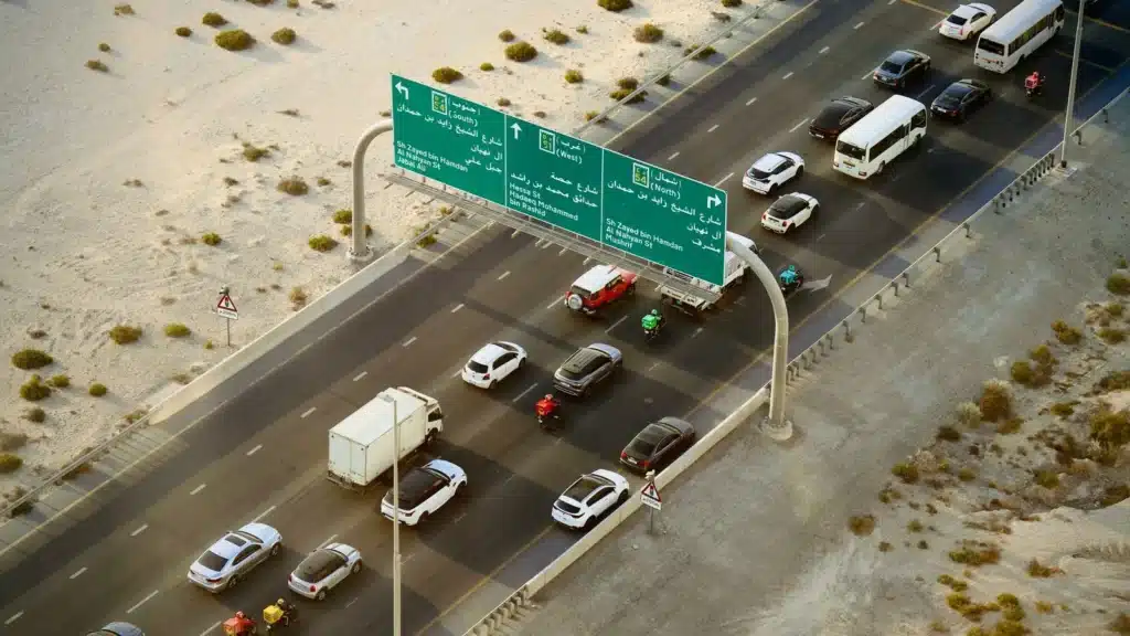 Aerial shot of vehicles on a busy highway in Dubai with road signs and desert surroundings.