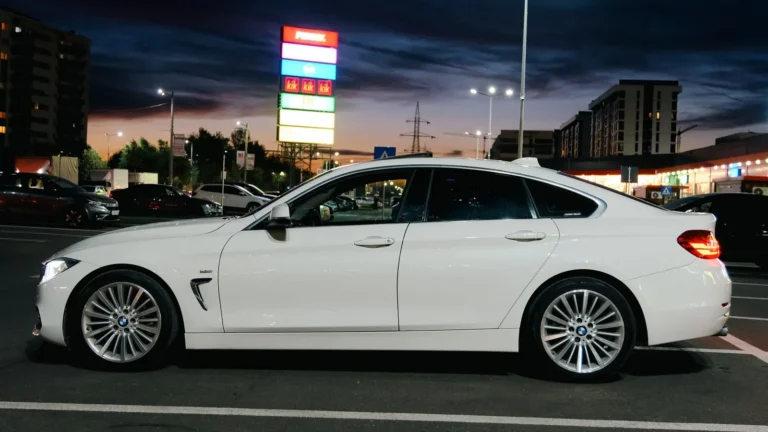 A sleek white sedan parked in an urban lot under evening lights.